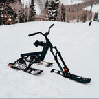 Black ski bike on a snowy landscape with mountains and trees in the background