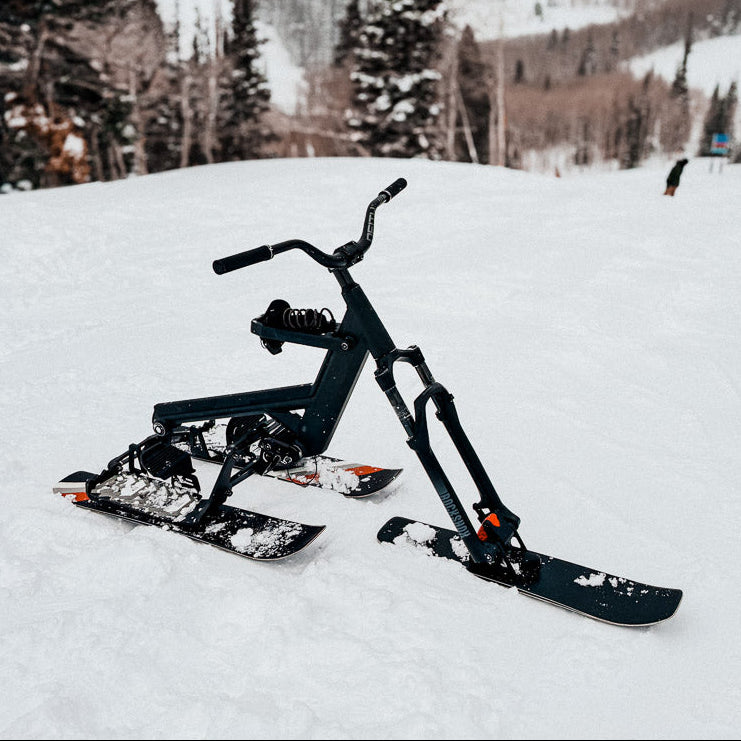 Black ski bike on a snowy landscape with mountains and trees in the background