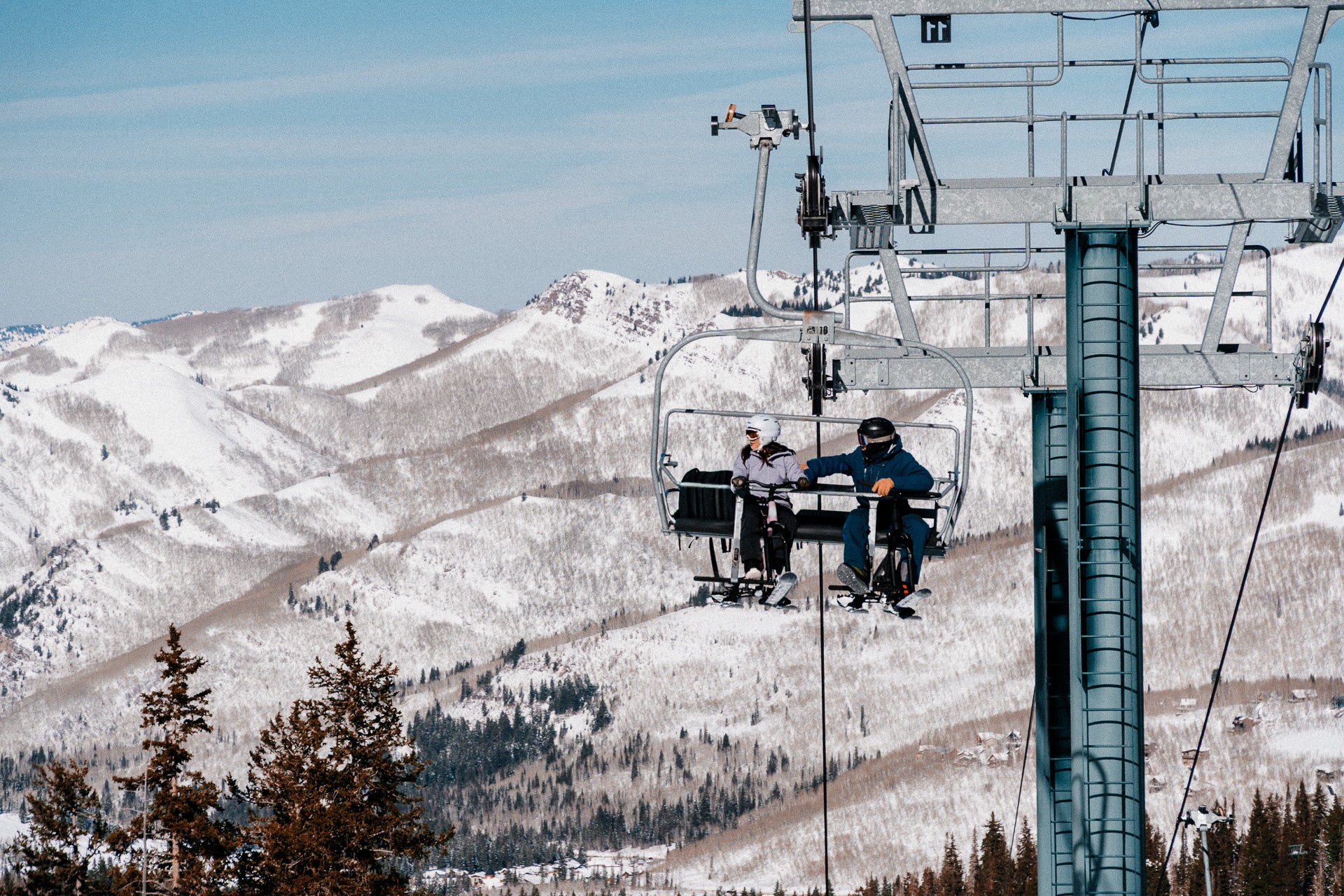 People riding ski bikes on a ski lift in Park City with snow-covered mountains in the background